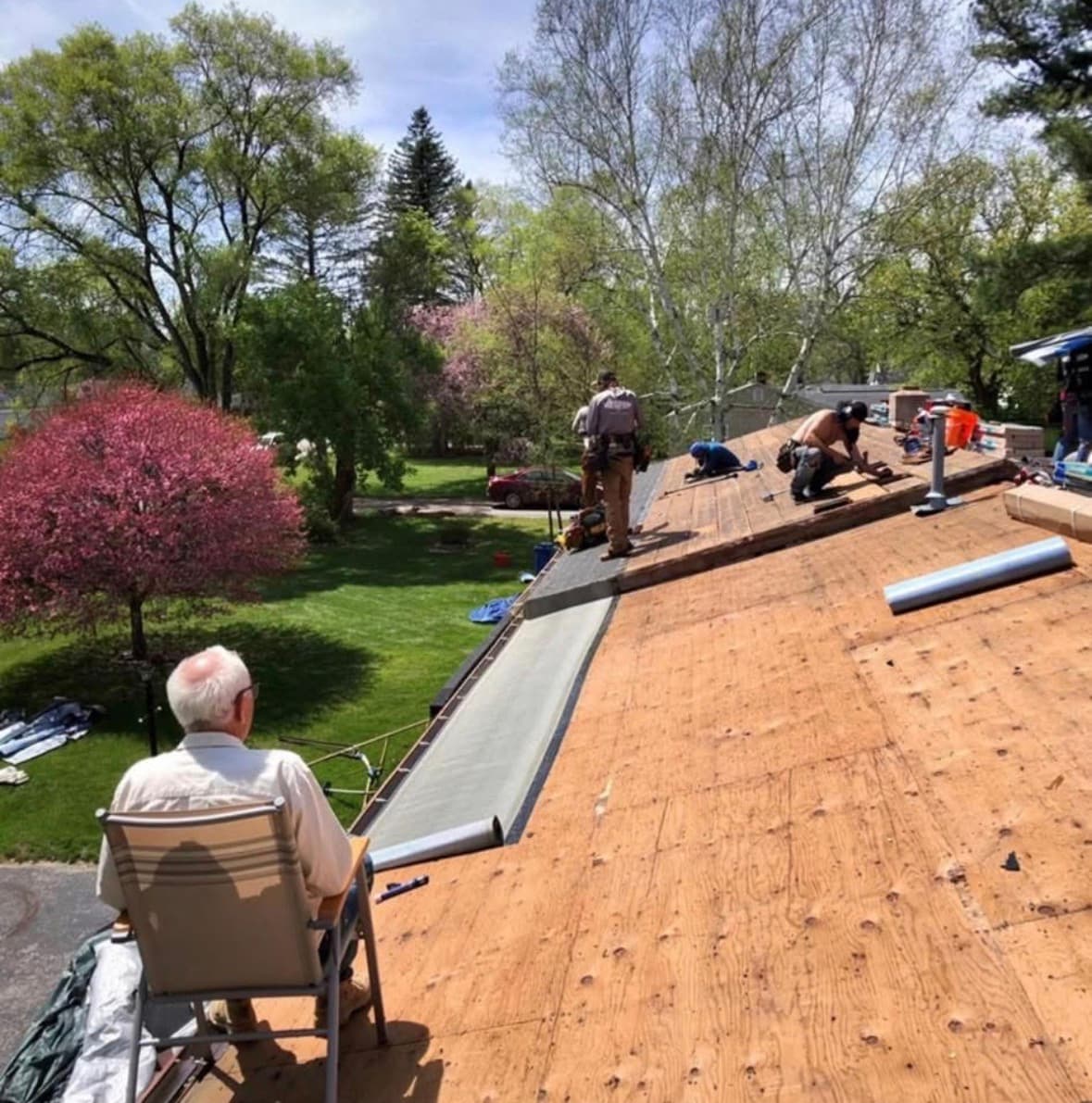 A homeowner sitting on the roof while the Essential Exteriors crew works nearby